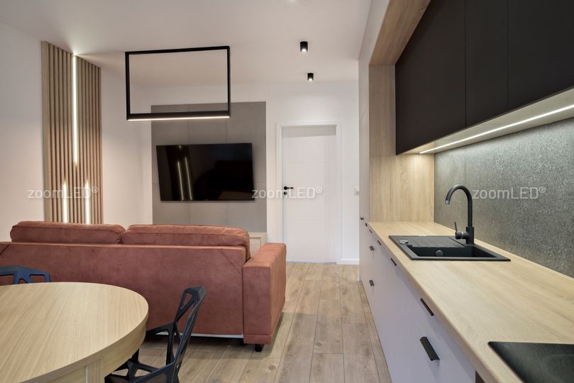 Małe mieszkanie zrobione z gustem, czarne lampy sufitowe, podświetlane lamele i szafki w kuchni